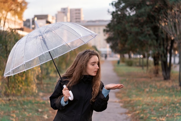 Portret młodej kobiety z długimi brązowymi włosami stojącej na zewnątrz i trzymającej parasol Dziewczyna z parasolem w pochmurny jesienny dzień