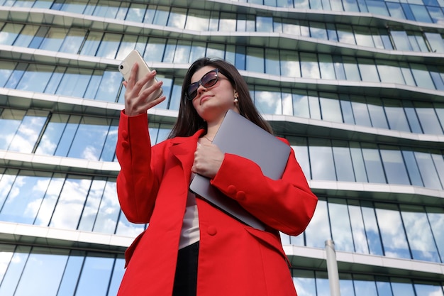 Portret młodej kobiety z laptopem i telefonem komórkowym na tle budynku