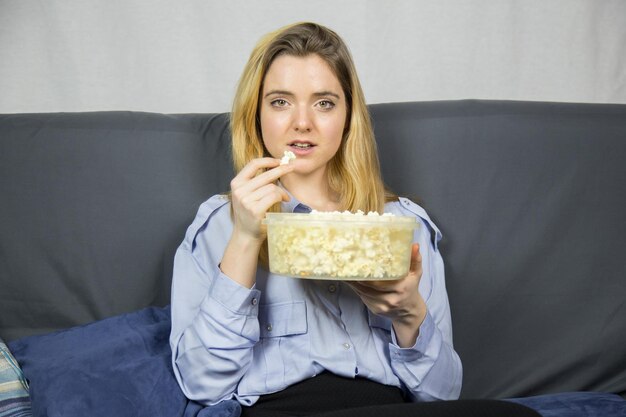 Zdjęcie portret młodej kobiety z popcornem siedzącej w domu na kanapie