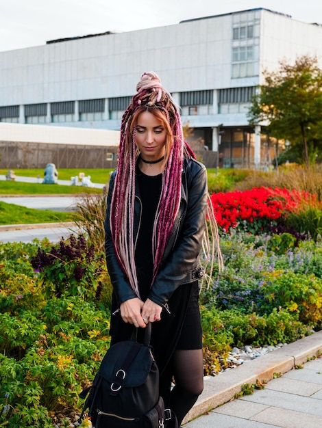 Portret Młodej Kobiety Z Różowymi Dredami W Czarnych Ubraniach Z Plecakiem Pozuje W Parku