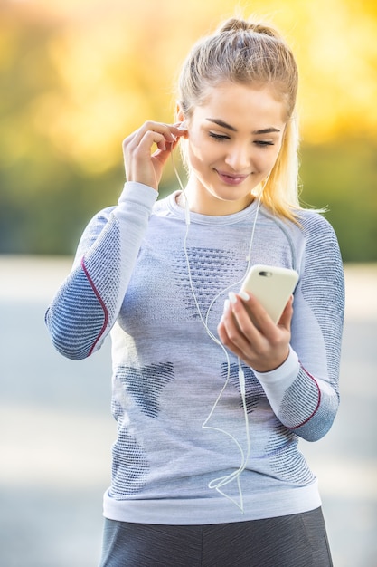 Portret młodej kobiety ze smartfonem i słuchawkami przygotowuje się do joggingu w jesiennym parku.