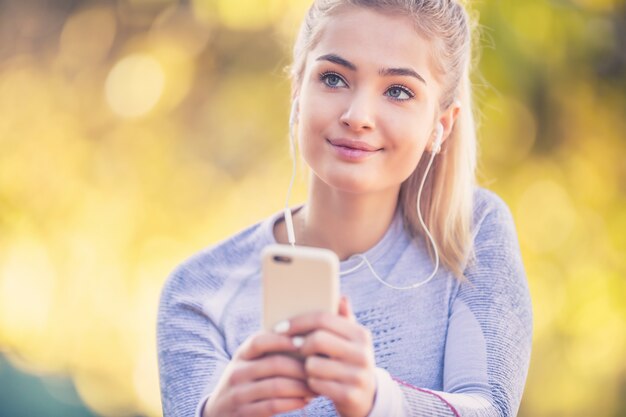 Portret Młodej Kobiety Ze Smartfonem I Słuchawkami Przygotowuje Się Do Joggingu W Jesiennym Parku.