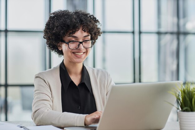 Zdjęcie portret młodej, odnoszącej sukcesy kaukaskiej bizneswoman siedzącej przy biurku i pracującej na laptopie