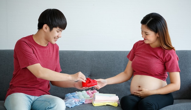 Portret młodej pary azjatyckich siedzi razem szczęśliwie na kanapie w domu, przygotowując noworodka w oczekiwaniu na dziecko. Spodziewając się zdrowej koncepcji dziecka.