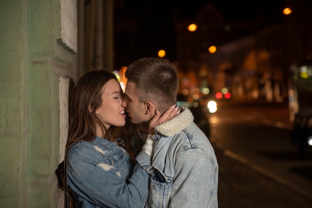 Portret młodej pary całuje na tle miasta w nocy. Romantyczna data. młoda para w miłości. Piękna dziewczyna przytula faceta.