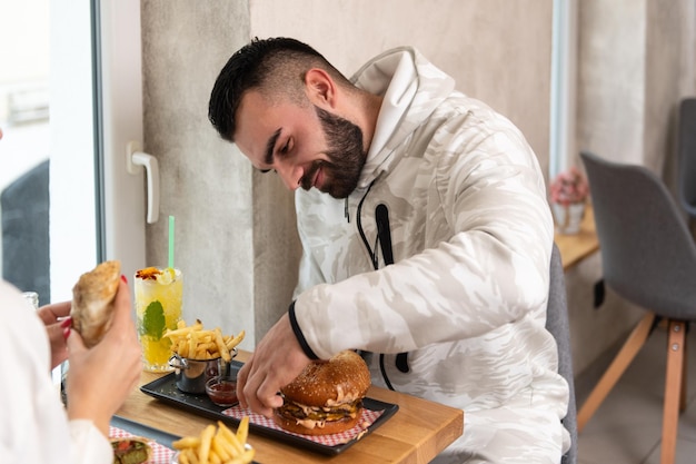 Portret młodej pary jedzącej hamburgera w restauracji i pijącej koktajl z marakui Mojito