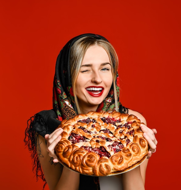 Portret młodej pięknej blondynki w chuście na głowie trzymającej pyszne domowe ciasto jagodowe