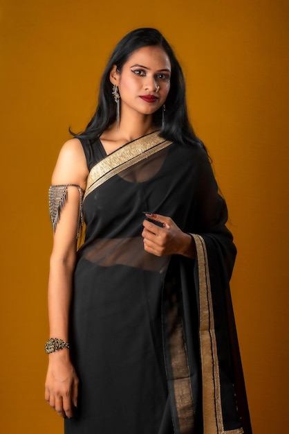 Portret młodej pięknej dziewczyny ubranej w tradycyjną czarną sari pozującą na brązowym tle
