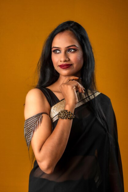 Portret młodej pięknej dziewczyny ubranej w tradycyjną czarną sari pozującą na brązowym tle
