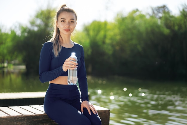 Portret młodej pięknej kobiety noszącej niebieską odzież sportową wodę pitną w parku