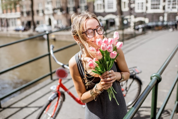 Portret młodej pięknej kobiety stojącej z bukietem różowych tulipanów na moście na starym mieście w Amsterdamie