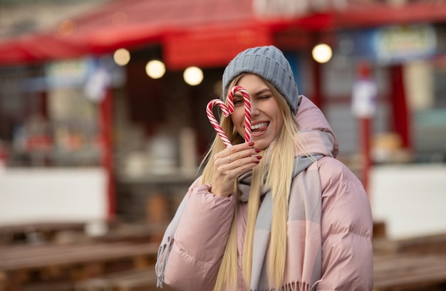 Portret młodej pięknej kobiety szczęśliwy z cukierków pozowanie na ulicy w europejskim mieście. Boże Narodzenie.