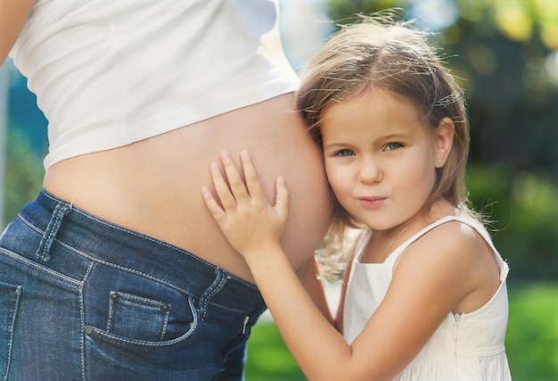 Zdjęcie portret młodej pięknej kobiety w ciąży z małą dziewczynką w białych ubraniach