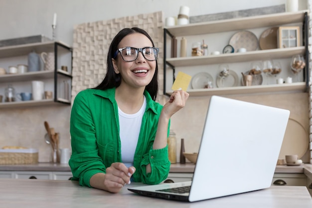 Portret młodej pięknej kobiety w okularach w domu w kuchni brunetki za pomocą laptopa do Internetu