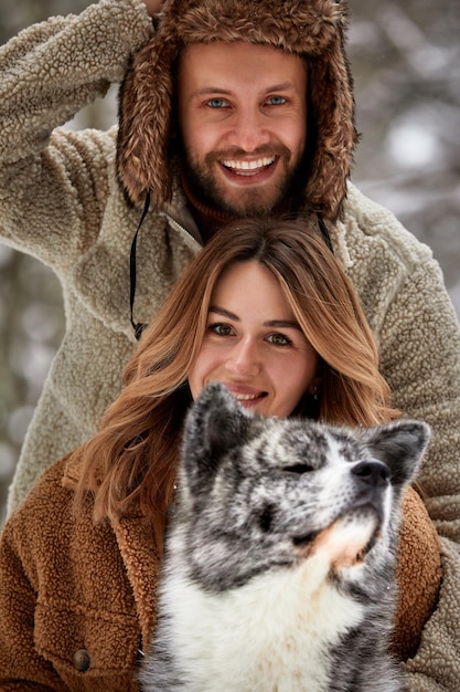 Portret młodej pięknej pary o europejskim wyglądzie z psem husky w zimowym lesie