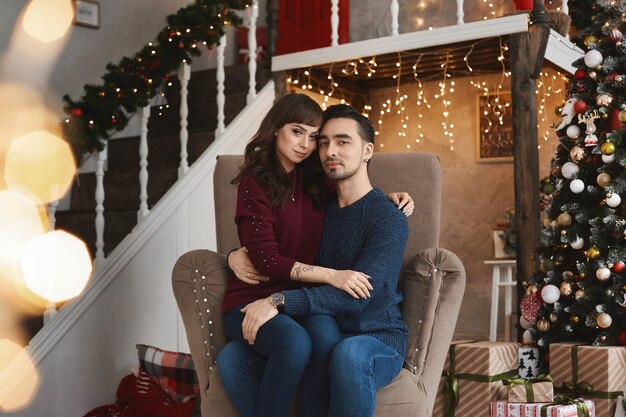 Portret młodej pięknej pary siedzącej w fotelu w salonie w czasie świąt Bożego Narodzenia