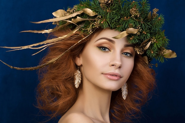 Portret młodej pięknej rudowłosej kobiety z jodłowym wieńcem ze złotymi liśćmi we włosach.