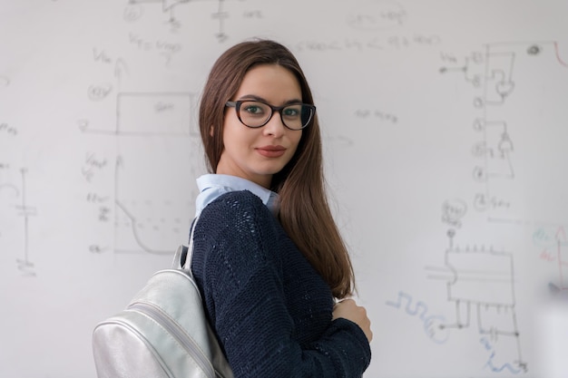 portret młodej pięknej studentki stojącej przed białą tablicą i patrzącej w kamerę