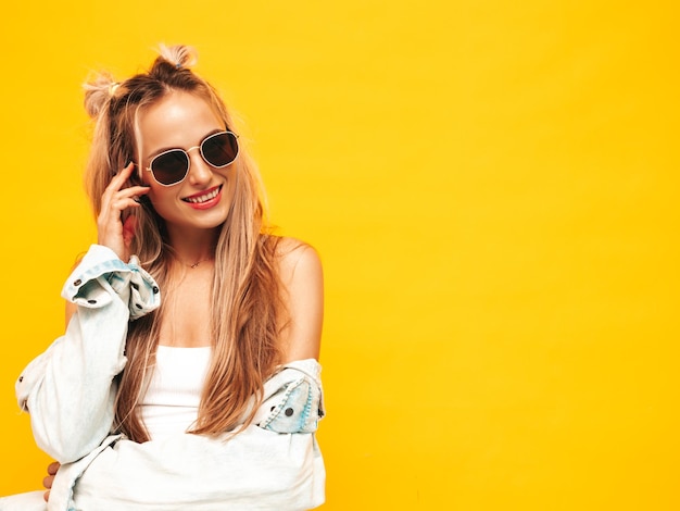 Portret młodej pięknej uśmiechniętej blond kobiety w modnych letnich ubraniach Seksowna beztroska kobieta pozuje w pobliżu żółtej ściany w studio Pozytywny model zabawy w pomieszczeniu Wesoły i szczęśliwy w okularach przeciwsłonecznych