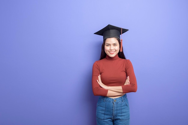 Zdjęcie portret młodej studentki uniwersytetu w czapce dyplomowej na fioletowym tle