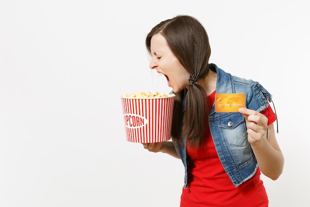 Portret Młodej Szalonej Wariatki Brunetka W Ubraniach Casual, Oglądanie Filmu, Trzymając Wiadro Popcornu I Karty Kredytowej, Krzycząc Na Białym Tle. Emocje W Koncepcji Kina.