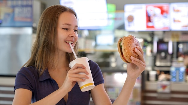 Zdjęcie portret młodej szczęśliwej kobiety lub pięknej nastoletniej dziewczyny jedzącej szybkie śmieciowe jedzenie smaczny hamburger i