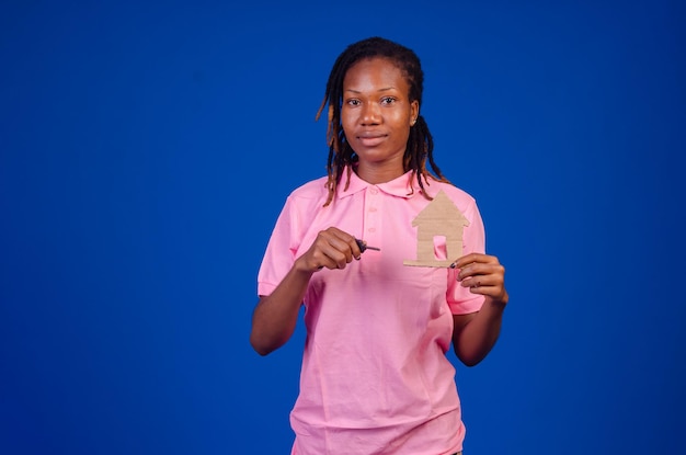 Portret młodej szczęśliwej uśmiechniętej afroamerykańskiej kobiety trzymającej papierowy dom dla koncepcji nieruchomości