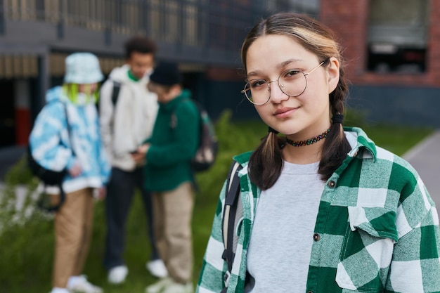 Zdjęcie portret młodej uczennicy w okularach i koszuli w kratę, patrząc w kamerę, stojąc na zewnątrz