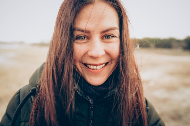 Portret młodej uśmiechniętej brunetki w zimnej kurtce patrzącej na kamerę