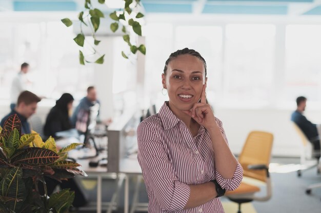 Portret młodej uśmiechniętej kobiety biznesu w biurze startowym kreatywnej otwartej przestrzeni coworkingowej. Pomyślna bizneswoman stojąca w biurze z copyspace. Współpracownicy pracujący w tle.