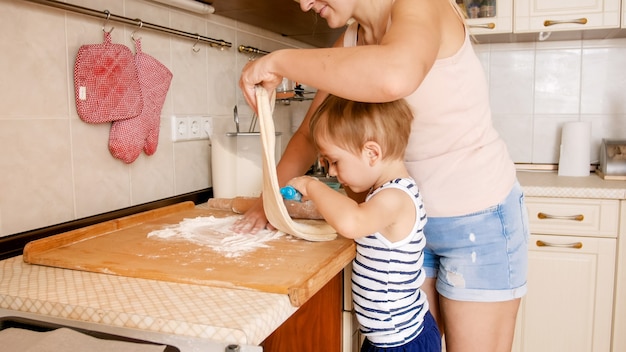 Portret młodej uśmiechniętej matki uczy swojego 3-letniego chłopca pieczenia i robienia ciasteczek w kuchni