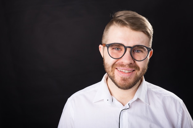 Portret młodej uśmiechnięty brodaty mężczyzna w okularach na czarnym tle z miejsca na kopię