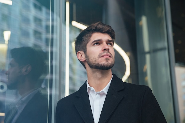 portret młody atrakcyjny biznesmen ubrany w oficjalną odzież stojącą w pobliżu centrum biznesowego i patrzeć na bok.