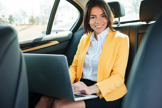 Portret młody bizneswoman z laptopem na tylnym siedzeniu w samochodzie