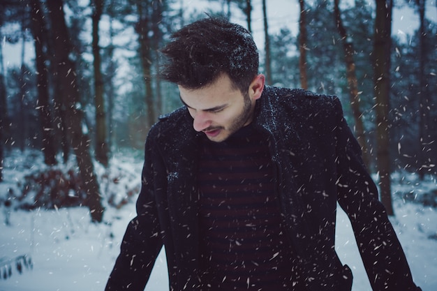 Portret młody człowiek pozycja w lesie podczas śnieżnej burzy