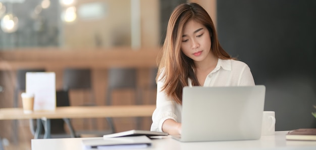 Portret młody piękny azjatykci bizneswoman pracuje nad jej projektem podczas gdy pisać na maszynie na laptopie