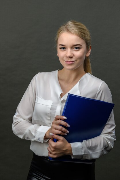 Portret młody piękny blondynka bizneswoman trzyma błękitną falcówkę na szarym tle.