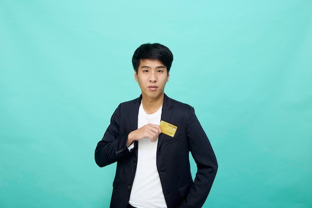 Portret Młody przystojny biznesmen w garniturze z żółtą kartą kredytową na białym tle w niebieskim studio