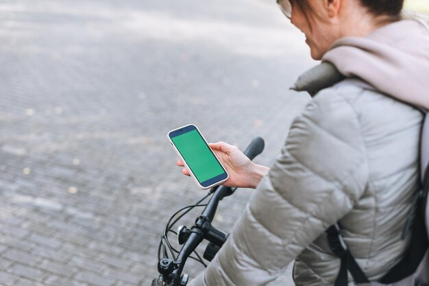 Portret Modnej Szczęśliwej Młodej ładnej Kobiety W Czapce I Okularach Przeciwsłonecznych Za Pomocą Telefonu Komórkowego Na Rowerze W Słoneczny Jesienny Dzień W Parku Miejskim Makieta Mobilna Smartphone Z Zielonym Ekranem