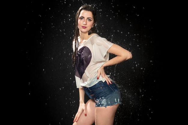 Portret Mokrej Seksownej Kobiety W Koszulce I Szortach Pod Kroplami Wody Na Czarnym Tle