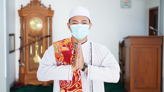 Portret muzułmańskiego mężczyzny z Azji wznosi się w powitalnej pozie do rąk Namaste, witając gości, Ied Fitr wita w meczecie. Noszenie maski