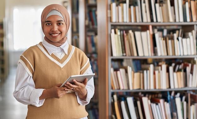 Portret muzułmańskiego studenta uśmiechającego się do kamery podczas korzystania z komputera typu tablet w bibliotece