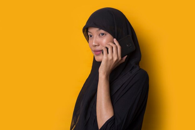 Portret muzułmańskiej dziewczyny za pomocą smartfona na żółtym tle