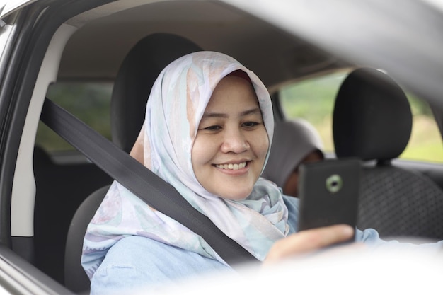 Portret muzułmańskiej kierowcy uśmiechającej się szczęśliwie patrząc na swój telefon w pojeździe samochodowym