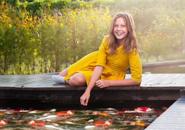 Portret nastolatka na moście. Dziewczyna karmiąca ryby w stawie