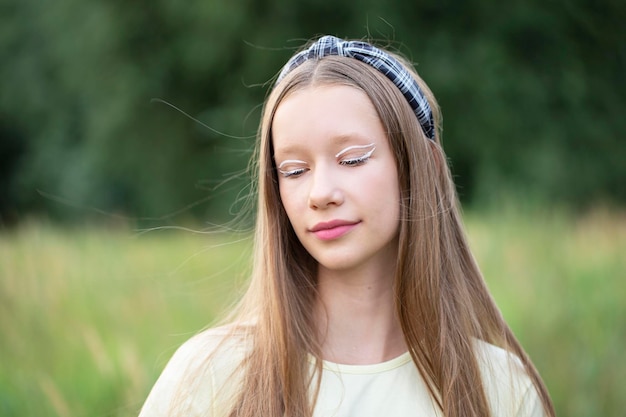 Portret nastolatki z kreatywnym makijażem i długimi blond włosami na tle natury