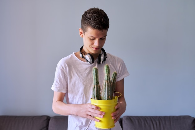 Portret nastoletniego chłopca 16 lat w słuchawkach, trzymając w rękach garnek kaktusów, szare tło
