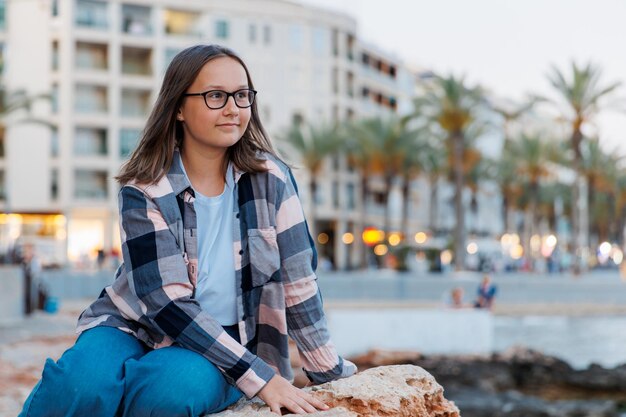 Portret nastoletniej dziewczyny w okularach na tle nabrzeża miasta w letni wieczór