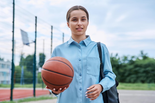 Portret nastoletniej studentki z plecakiem i piłką koszykarską patrzącej na kamerę w pobliżu boiska zewnętrznego szkoły koszykarskiej Aktywny zdrowy styl życia sportowy koncepcja szkoły dla nastolatków