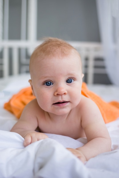 Portret niebieskookiego dziecka leżącego pod pomarańczowym ręcznikiem na łóżku